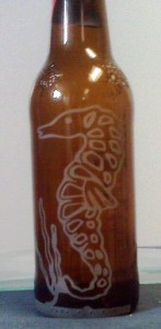 An etching of a sea horse on a beer bottle.