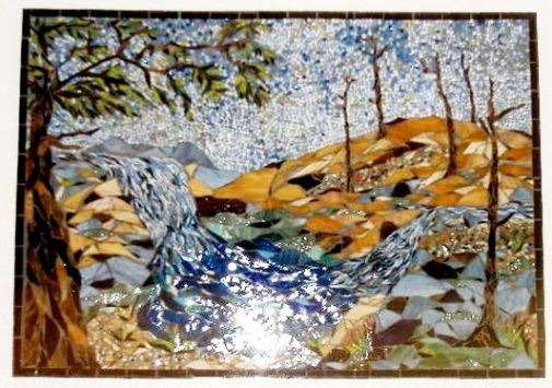 A stained glass portrait art of a waterfall scene on a piece of scrap wood.